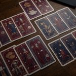 Plusieurs cartes de tarot identiques disposées en motif répétitif sur un bureau en bois sombre, évoquant une réflexion sur les thèmes récurrents dans le travail.